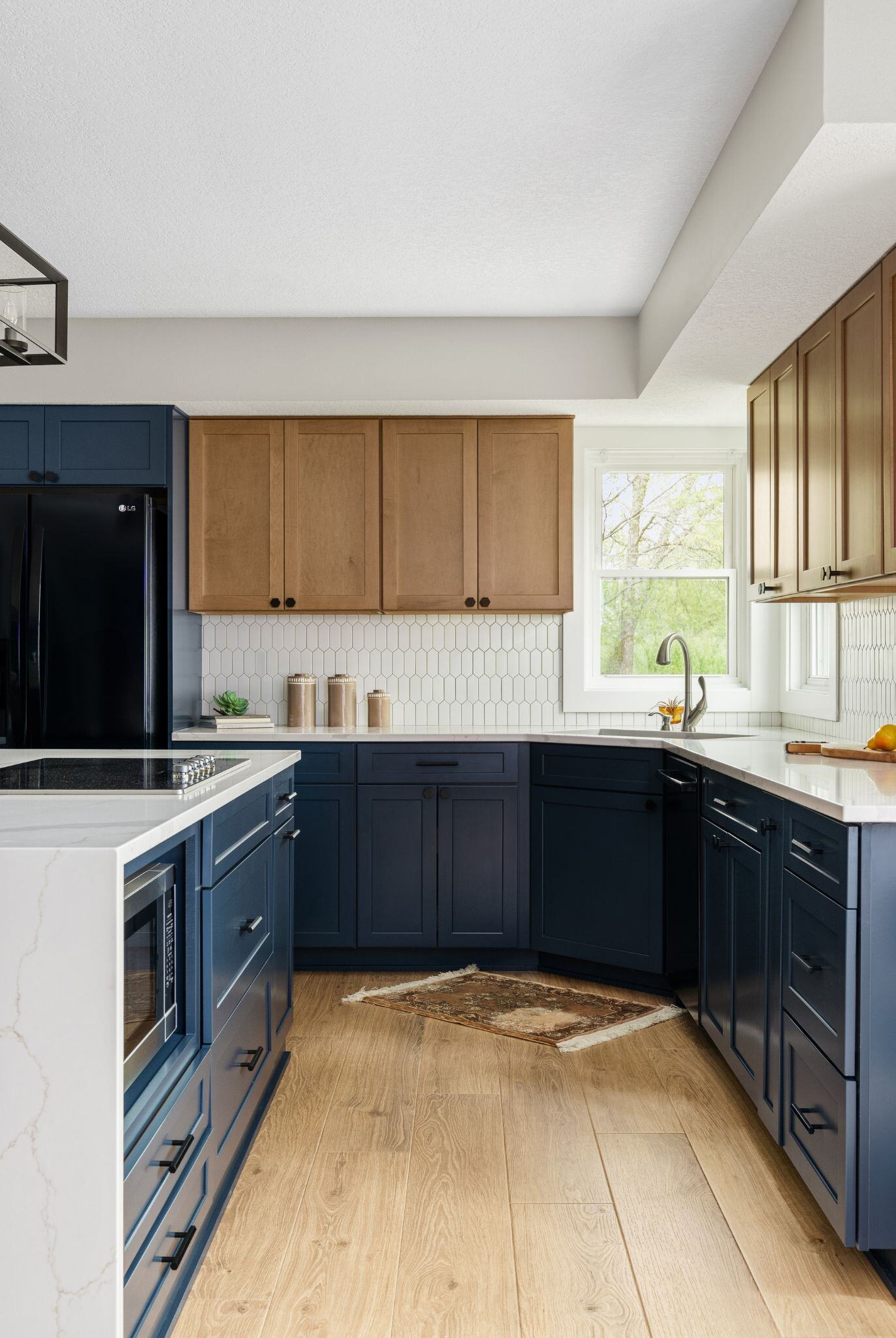 Kitchen remodel in Des Moines with dark blue cabinets, white counters and backsplash, and light wood flooring