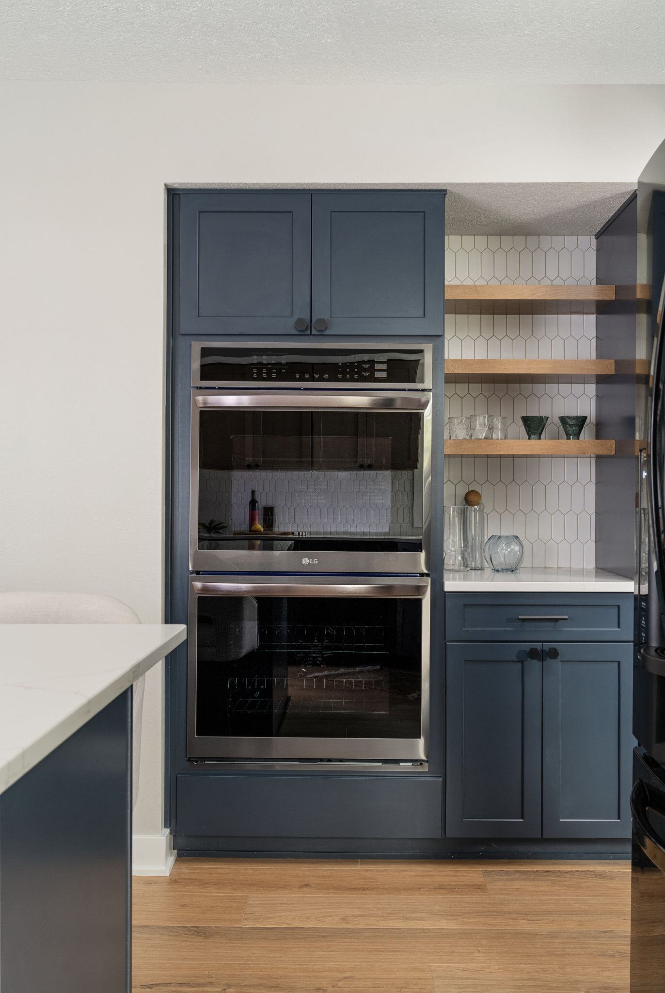 Kitchen remodel in Des Moines with dark blue cabinets, white counters and backsplash, and light wood flooring and stainless steel double oven