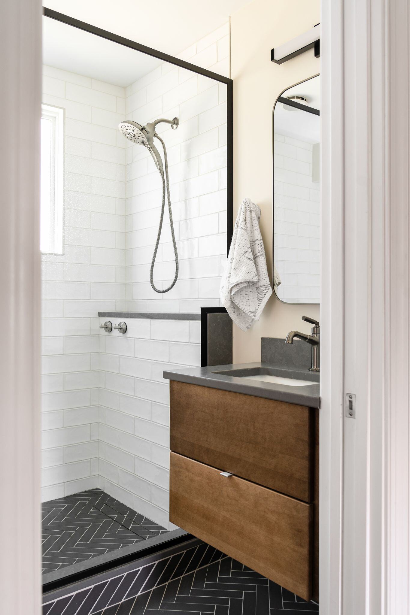 bathroom remodel in des moines with herringbone bathroom tile in a black color and a floating vanity with organic finishes