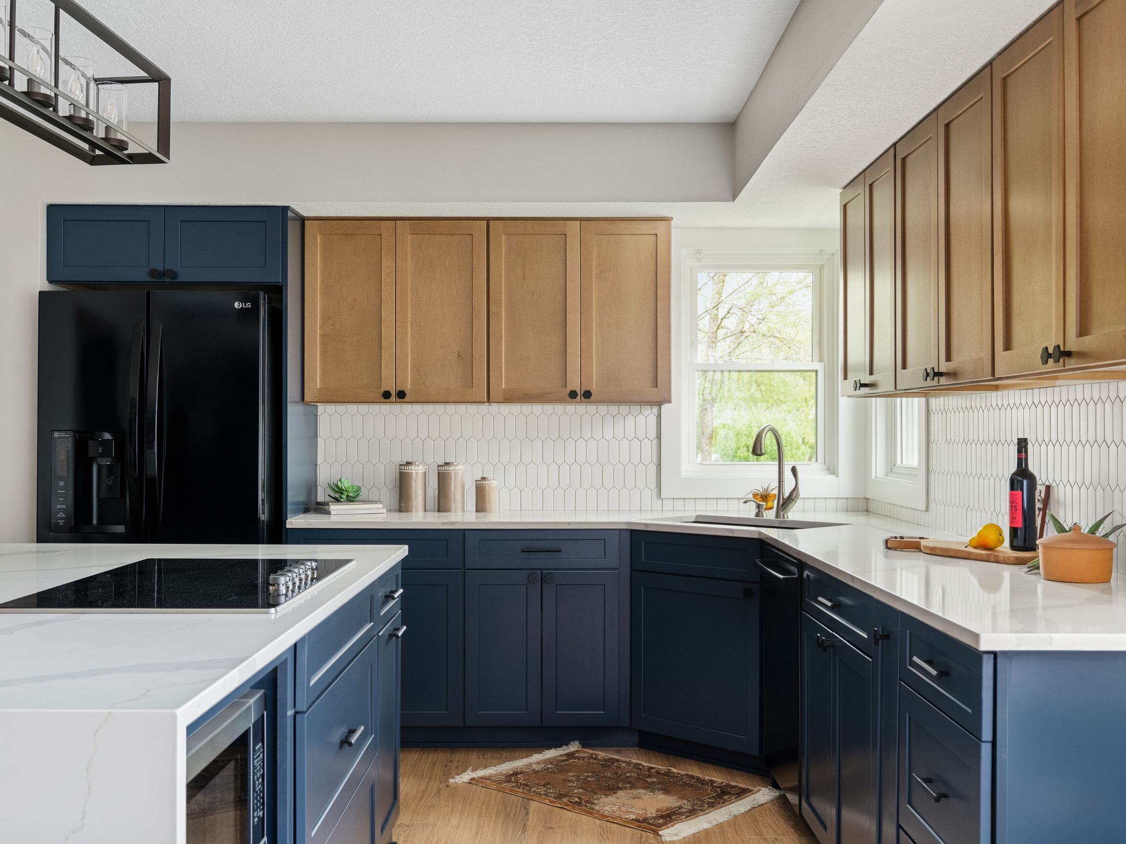 Dark blue cabinets with light wood floors and white countertops and backsplash in a remodeled kitchen in Des Moines