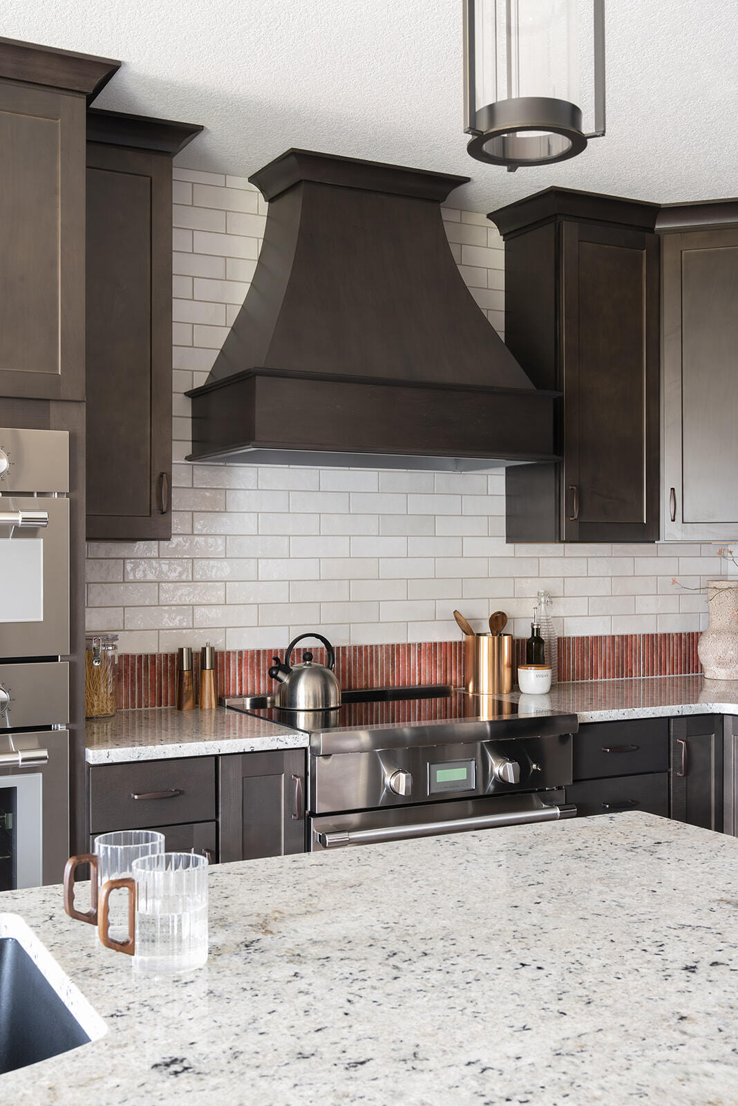 Kitchen remodel with custom dark cabinets and vent hood and white countertops and backsplash with orange accent.