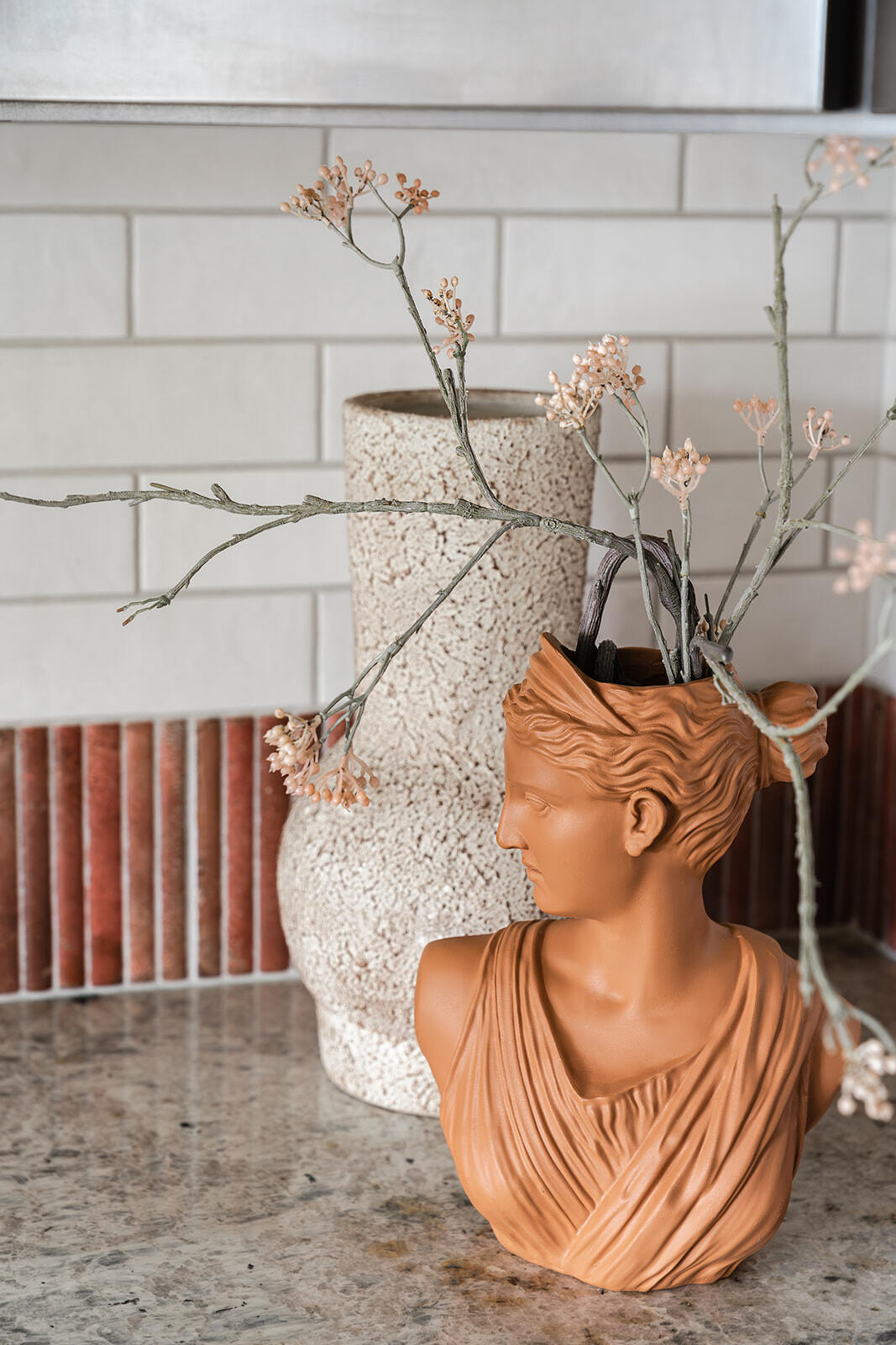 Detail shot of statuette vase and cylindrical case against custom white subway tile and coral kitchen backsplash