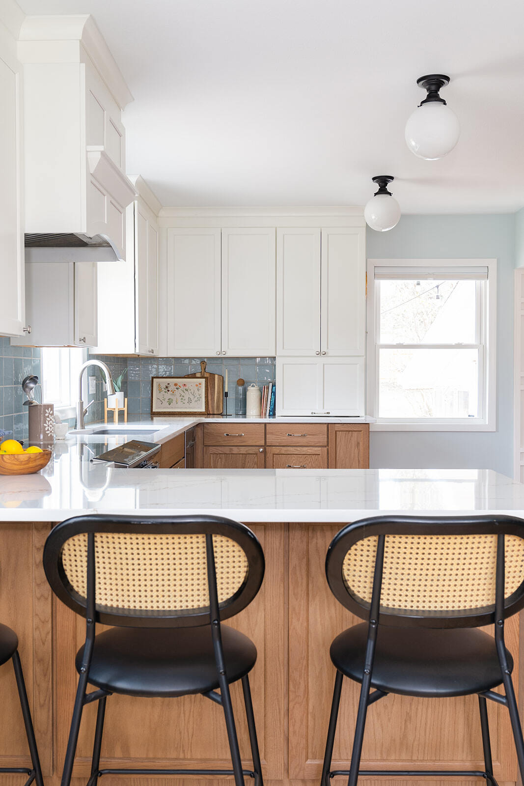 Close up image of remodeled kitchen with bar stools, wooden and white kitchen cabinets, and white counter