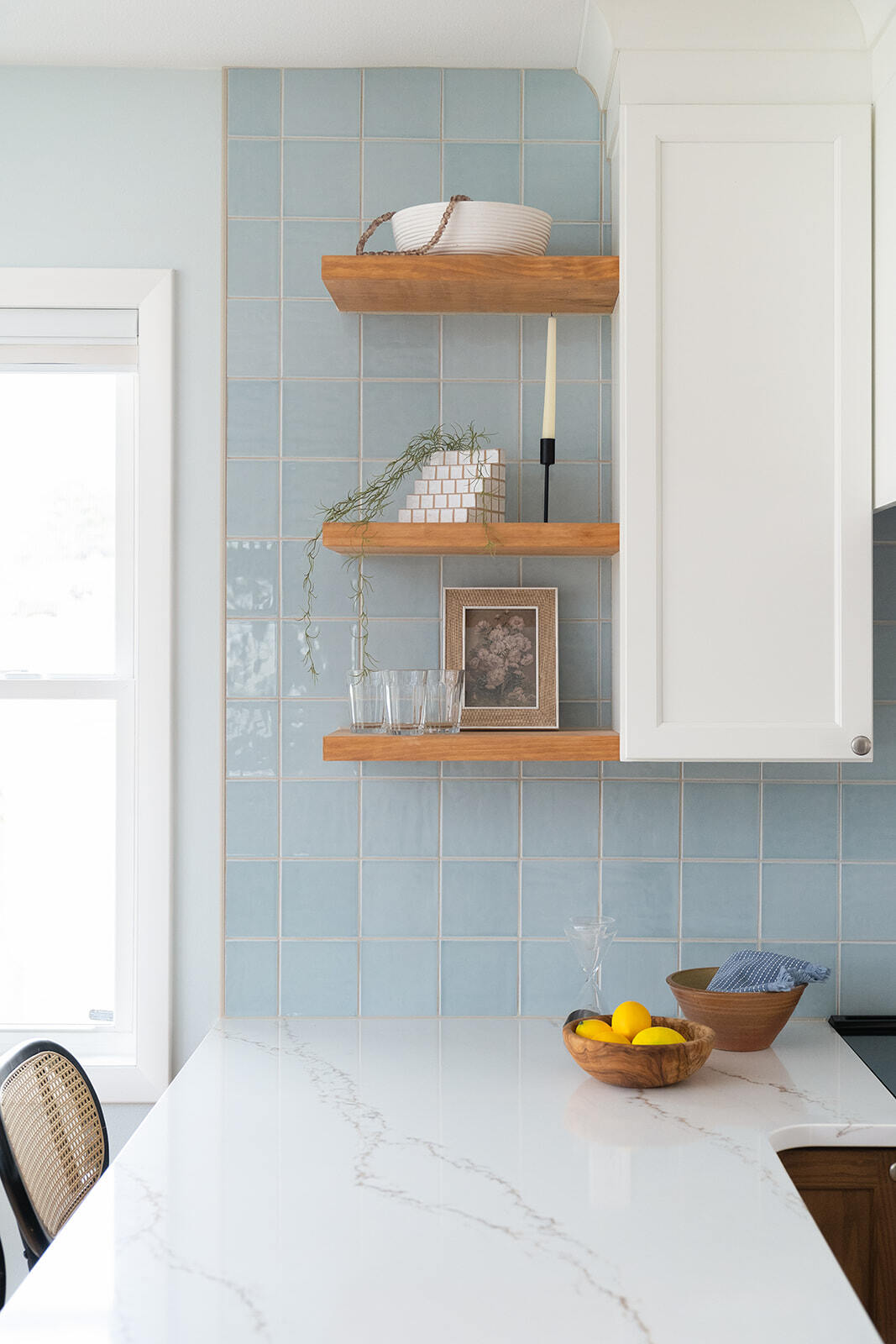 Kitchen remodel in Des Moines featuring white granite countertop, square blue backsplash, and wooden shelving