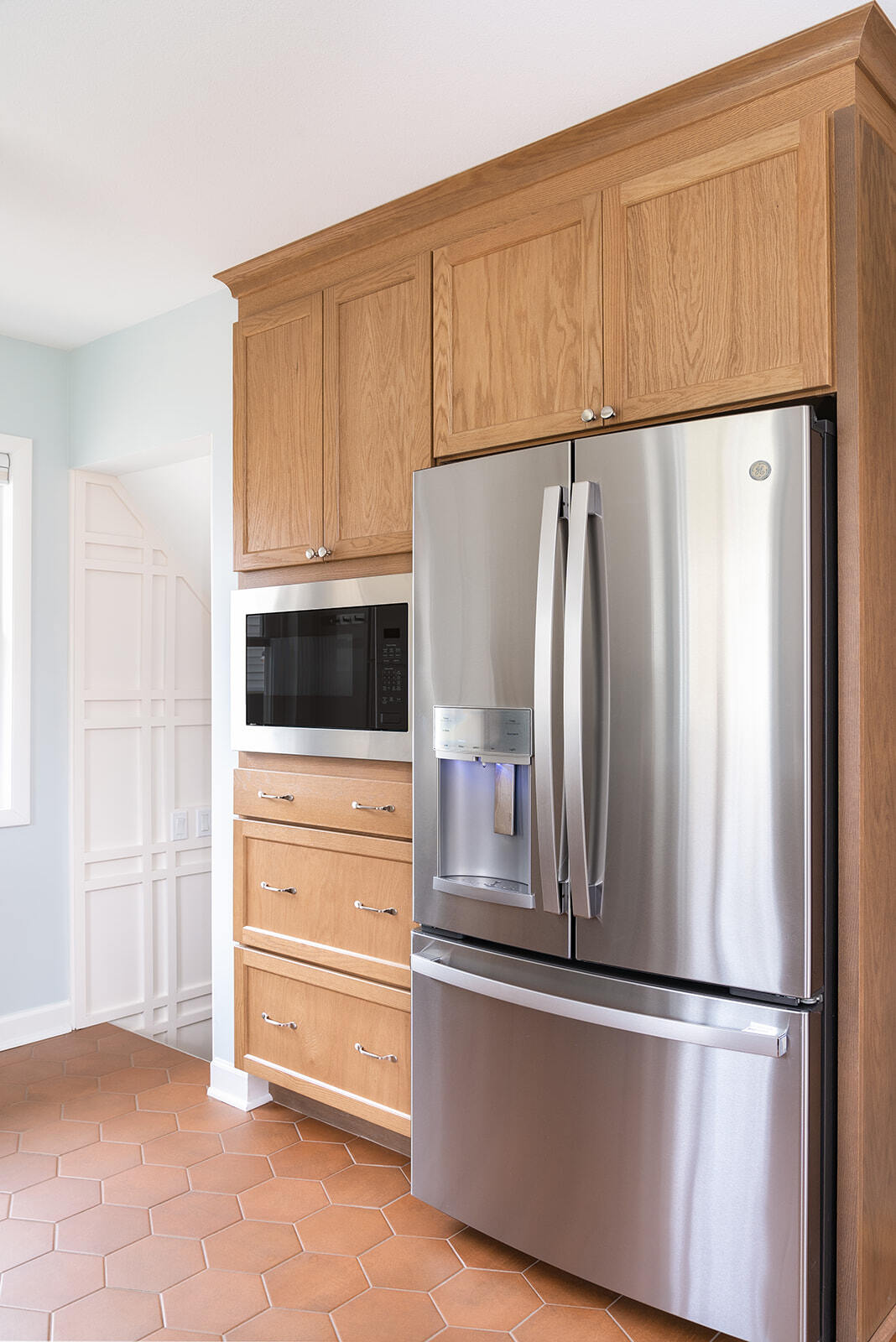 Remodeled kitchen with stainless steel fridge and microwave, wooden cabinets, and red clay floor tiles