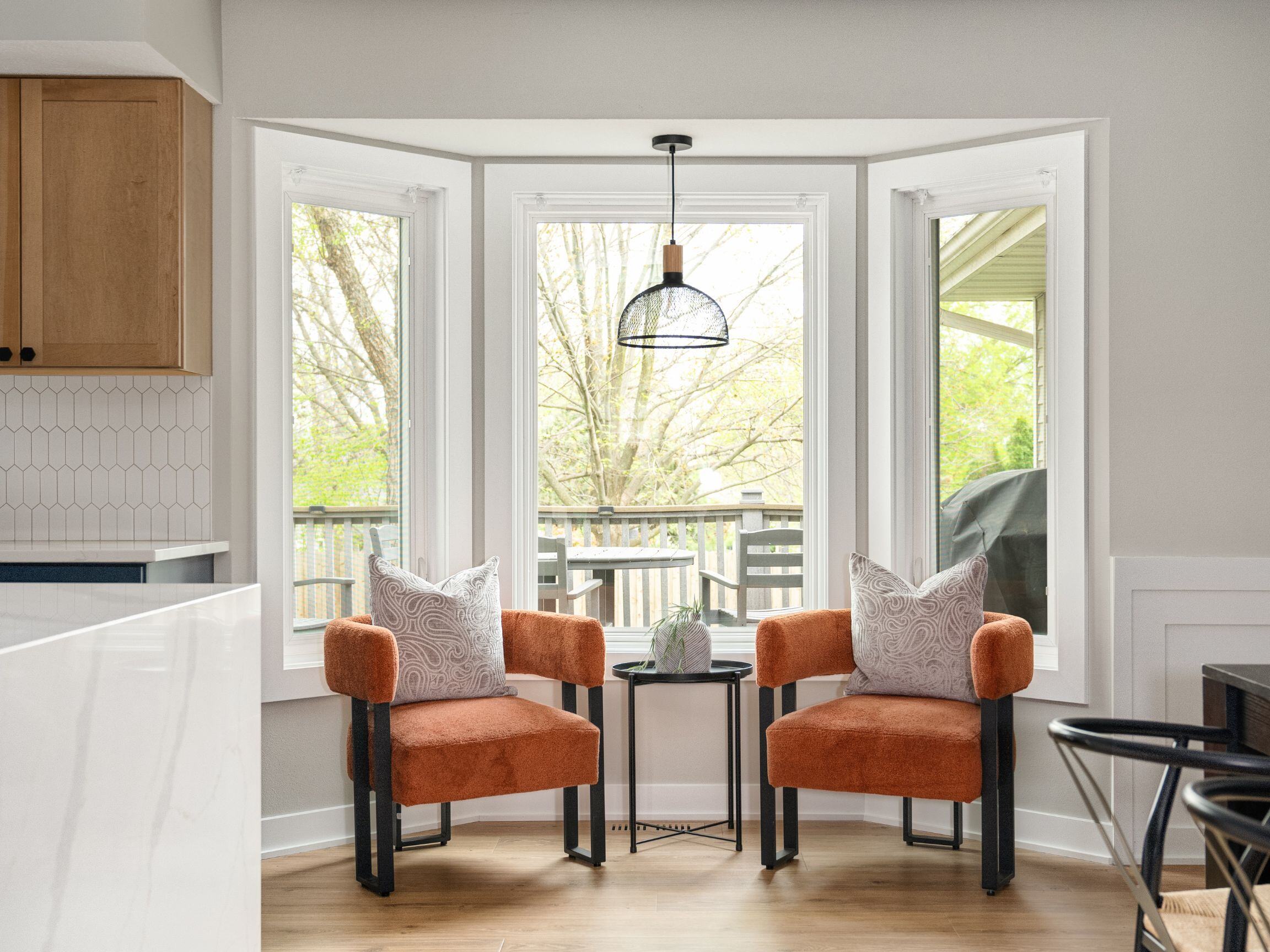 Two orange arm chairs in a breakfast nook in front of a window in a remodeled kitchen with light wood floor